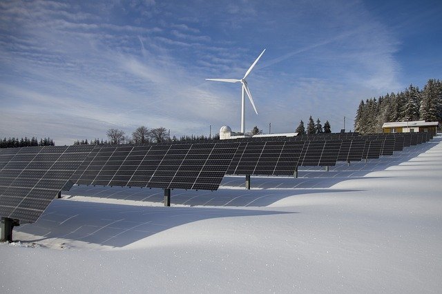 Solpaneler och ett vindkraftverk tillsammans i ett snöigt landskap.